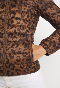 Giacca puffer marrone con un motivo a stampa leopardata. Presenta una chiusura frontale con zip e polsini elasticizzati, realizzata in un materiale lucido e morbido.