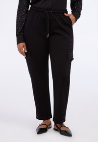 Pantaloni neri realizzati in un tessuto morbido con una vestibilità rilassata, con toppe decorative di paillettes sui taschini anteriori e una cintura elastica.