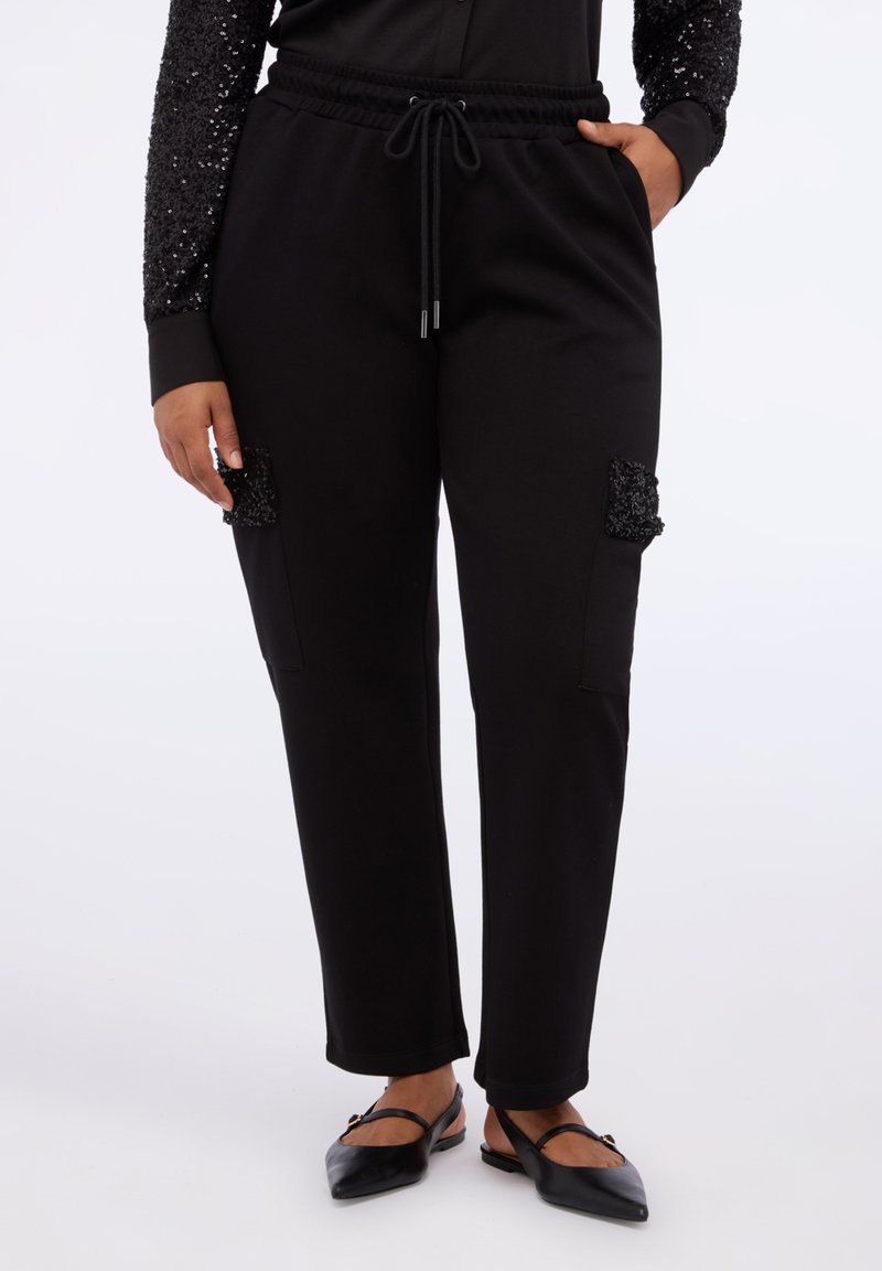 Pantaloni neri realizzati in un tessuto morbido con una vestibilità rilassata, con toppe decorative di paillettes sui taschini anteriori e una cintura elastica.