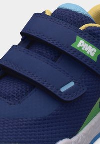 Μπλε παιδικό αθλητικό παπούτσι με ύφασμα από δίχτυ, δύο ιμάντες βέλκρο, πράσινη και λευκή ετικέτα λογότυπου, και γαλάζιες και κίτρινες λεπτομέρειες.