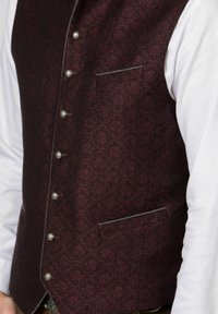 Burgunderfarbene gemusterte Weste mit silbernen Beschlägen, einer Brusttasche und grauen Paspeldetails, getragen über einem weißen Hemd.
