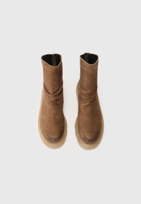 Bottes en cuir marron à hauteur de cheville avec un design décontracté, présentant une texture lisse, un bout arrondi et une semelle marron clair contrastante.