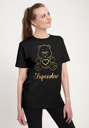 Zwarte T-shirt met een gouden beer grafiek met een hart, en het woord "Superster" in een cursieve lettertype eronder. Zacht fabric, relaxte pasvorm.