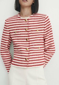 Veste courte rayée rouge et blanche en tissu texturé, dotée de boutons dorés et d'un col rond.