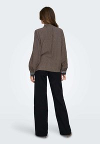 Blusa a maglia marrone con un motivo geometrico, dotata di un alto colletto e maniche voluminose. Abbinata a pantaloni neri a gamba larga.
