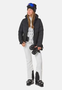 Zwarte pufferjack, gestreepte witte trui, witte skibroek met zwarte accenten, zwarte handschoenen en skischaatsen, accessoires omvatten een skibril en een beanie.