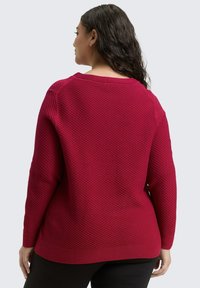 Roter strukturierter Pullover mit Rundhalsausschnitt und langen Ärmeln, der ein rautenförmiges Strickmuster sowie einen gerippten Saum und Ärmelsäume aufweist.