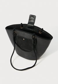Borsa tote nera con una finitura texturizzata, dettagli in suede e una tasca frontale. Presenta due maniglie in tessuto e una forma ampia e strutturata.