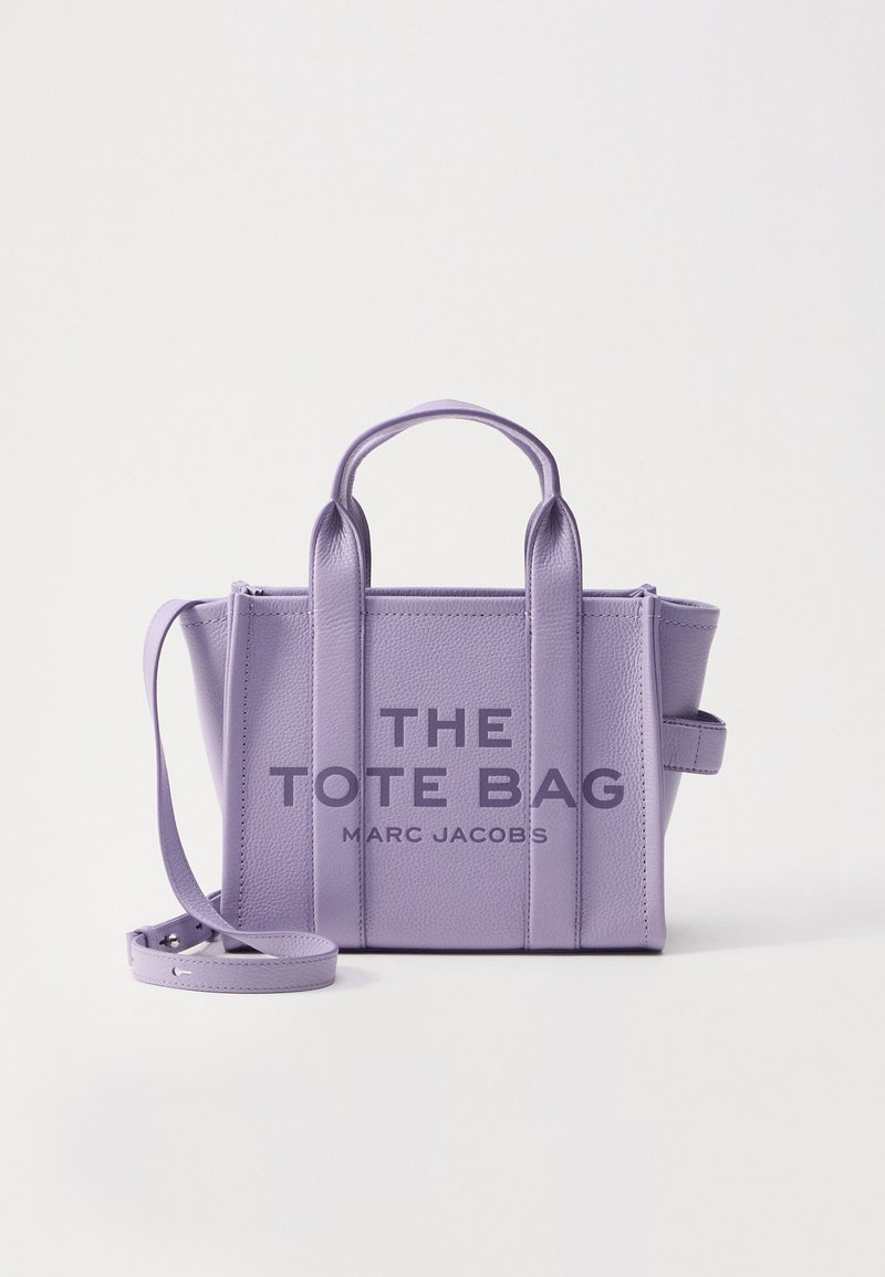Bolsa tote de couro lavanda com duas alças superiores, uma alça de ombro destacável e "THE TOTE BAG MARC JACOBS" impresso na frente.