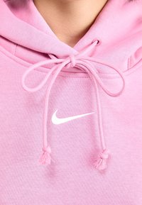 Närbild av en rosa Nike-hoodie med knutna dragsnören och vit Nike swoosh-logotyp på tyget.