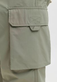 Oliwkowe szorty cargo z dużą, zakładaną kieszenią na rzep, teksturowaną tkaniną i wzmocnionymi szwami.