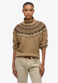 Suéter de punto marrón con cuello alto y una joroba con un patrón en tonos más oscuros, combinado con pantalones beige. El suéter tiene mangas arremangadas y un acabado texturizado.