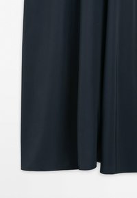 Donkerblauwe gordijn met zachte plooien hangend tegen een witte achtergrond, met een gladde stoftextuur aan de onderkant.