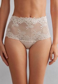 Las panties de encaje beige de cintura alta presentan patrones florales, bordes ondulados y una capa interior suave. El diseño combina transparencia y cobertura.