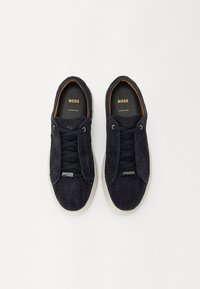 Mustat mokkasiinit, joissa on kudottu pinta, pyöreä kärki, sävyyn sopivat nauhat ja valkoinen kumipohja. Kulta "BOSS" -logo sisuspohjassa ja yksityiskohtia metallista.