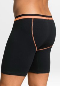 Boxer da uomo neri con un elastico arancione e cuciture in contrasto. Presentano un design aderente e una texture liscia senza motivi visibili.