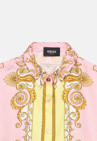Ružičasta bluza s uzorkom zlatnog baroka. Dizajn s ovratnikom i ukrasnim gumbom, kratki rukavi i svijetložuti prednji dio.