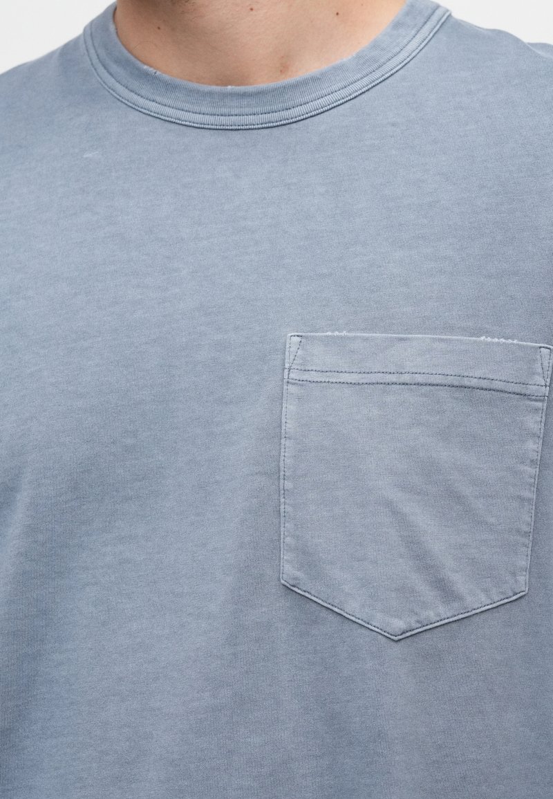 Ljusblå kortärmad t-shirt i mjukt tyg, med en liten bröstficka med sydd kant. Rund halsringning, slät textur.