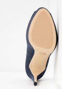 Décolleté con punta affilata, con tomaia in blu navy texture e suola beige, mostrato dalla vista inferiore su sfondo bianco.