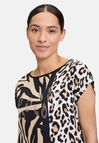 Haut à imprimé léopard avec des blocs de couleur noire, beige et blanche, texture lisse, manches courtes et embellissements en motif géométrique.