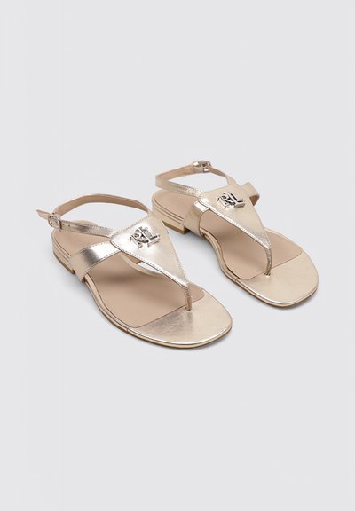 Sandales plates métalliques dorées avec bride à la cheville et logo "RL" sur la bride triangulaire à l'avant, présentées sur un fond gris clair uni.