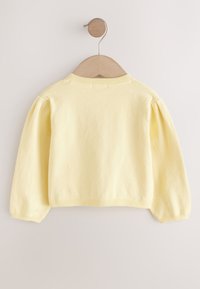 Gul strikket sweater med lange, puffede ærmer. Ribbet halsudskæring og kant, blødt materiale, ensfarvet design, og hænger på en træbøjle.