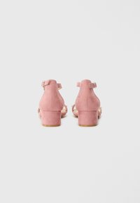 Rosa semskede blokkhæl sandaler med ankelremme, med en glat tekstur og minimal detaljering på en lys baggrund.
