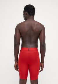Røde performance shorts med en glat tekstur, der har et tætsiddende design, midt-lår længde og en baglomme med en kontrasterende accent.