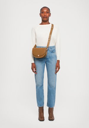 Brown crossbody bag with a curved flap, gold hardware, worn over a cream sweater and light blue jeans, paired with brown ankle boots.