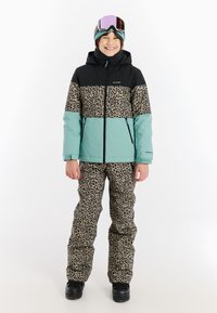 Giacca con stampa leopardata nera, turchese e leopardata; tessuto imbottito e impermeabile. Pantaloni abbinati con stampa leopardata; stivali neri. Completo da sci complessivo.