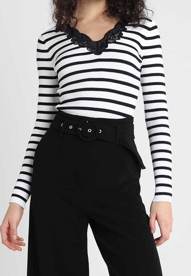 Haut côtelé à rayures noires et blanches avec un décolleté en V en dentelle, associé à un pantalon noir taille haute avec un détail de ceinture circulaire.