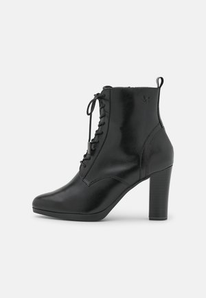 Bottine noire en cuir avec lacets, bout pointu et talon haut empilé, présentée de profil sur un fond uni.