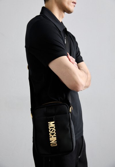 Geant�ă de umăr Moschino neagră, fabricată din nylon, cu un logo auriu, închidere cu fermoar și curea ajustabilă. Formă rectangulară cu textură căptușită.