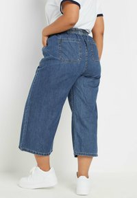 Denim culottes with an elastic waistband, dark blue color, wide legs, and two back pockets. Paired with white sneakers.
