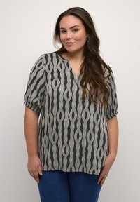 Blouse à motifs noir et blanc avec un col en V, des manches courtes bouffantes et une coupe ample. Le tissu présente des rayures ondulées allongées et une texture.