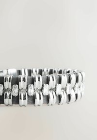 Sølvfarvet armbånd med skiftende glatte og matte led, der har rektangulære klare krystaller indlejret i et glat, mørkegråt bånd.