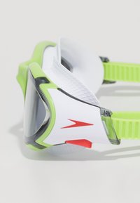 Zwembril met een witte montuur, groene accenten en donkere lenzen. Heeft gestructureerde zijkanten en een verstelbare band met rode hardware details.