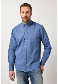 Camisa de color azul claro con botones, confeccionada en una tela texturizada, que incluye un bolsillo en el pecho y un cuello clásico, combinada con vaqueros claros de denim.