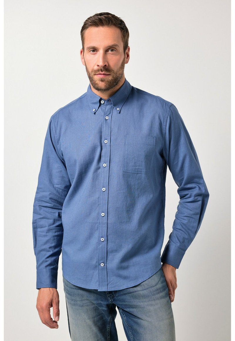 Camisa de color azul claro con botones, confeccionada en una tela texturizada, que incluye un bolsillo en el pecho y un cuello clásico, combinada con vaqueros claros de denim.