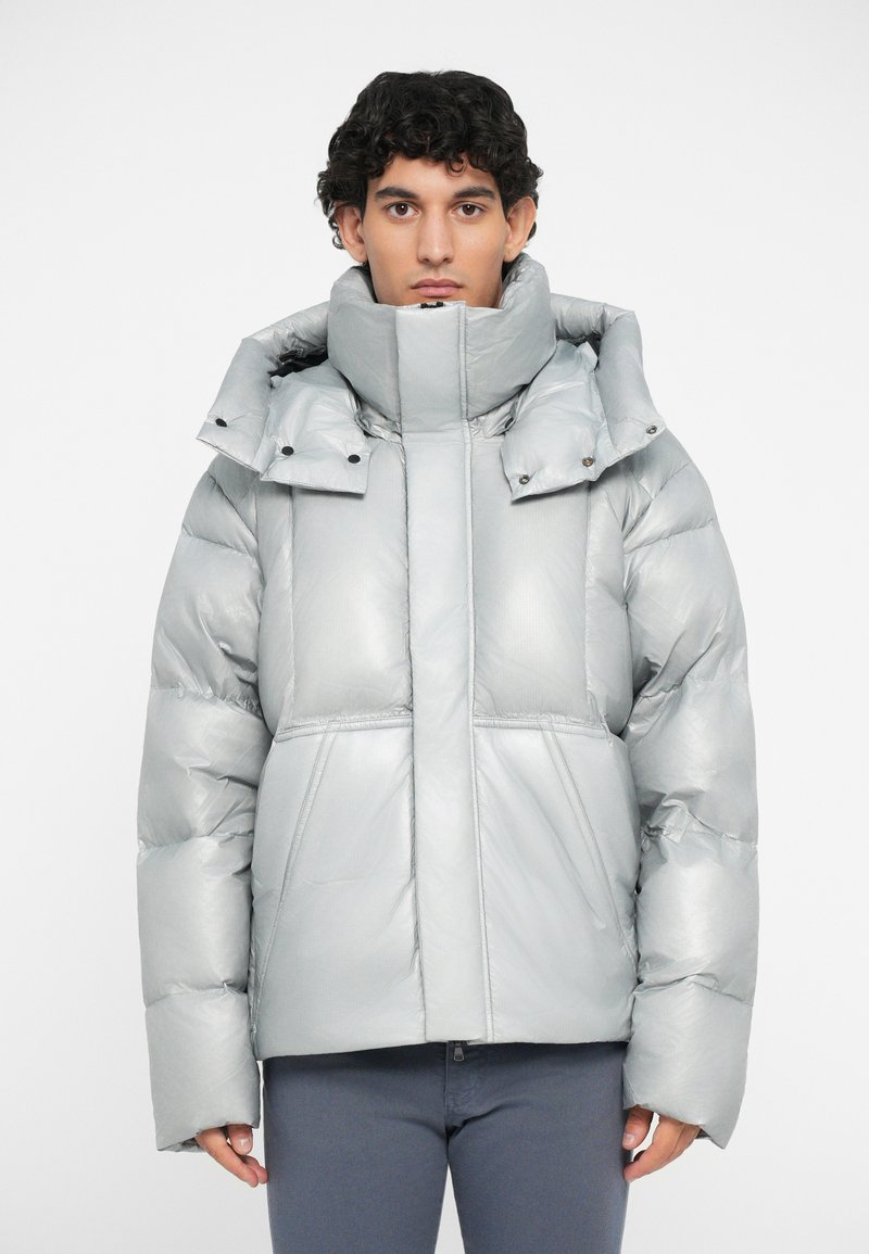 Metallic silver puffer jacket with a high collar, large hood, and snap buttons; features boxy design and quilted texture.