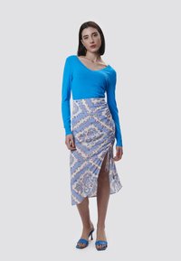 Blaues Langarmoberteil kombiniert mit einem gemusterten, hellblauen, knielangen Rock mit seitlichem Schlitz und Raffung. Blaue Absatzsandalen.