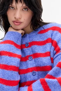 Πλεκτό ζακέτα με οριζόντιες μπλε και κόκκινες ρίγες, στρογγυλή λαιμόκοψη και κουμπιά σε μωβ. Μαλακή υφή με άνετη εφαρμογή.