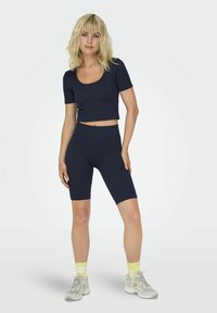Conjunto atlético de canalé en azul marino con un top corto de manga corta ajustado y unos pantalones cortos de ciclismo de cintura alta. Combinado con zapatillas deportivas grises y calcetines neón.