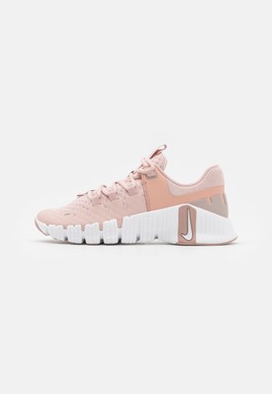 Zapatilla deportiva de color rosa claro con tejido transpirable, suela blanca segmentada, cordones y logo de Nike en la sección gruesa del talón.