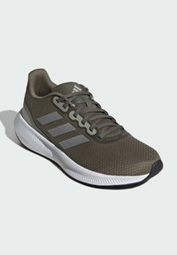 Zapato deportivo de color verde oscuro con parte superior de malla texturizada, detalles en gris, tres franjas reflectantes y suela de goma blanca.