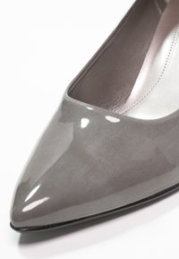 Chaussure pour femme à bout pointu en cuir verni gris brillant avec doublure intérieure rose pâle, présentée en gros plan sous un angle.