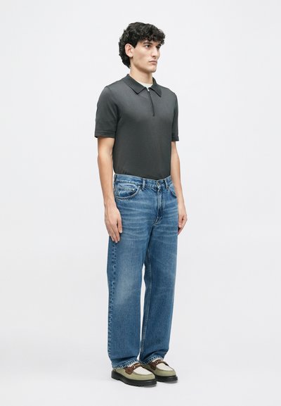 Sötét szürke, rövid ujjú pólóing, cipzáras záródással, világoskék, laza szabású farmernadrággal és zöld-barna alkalmi cipőkkel párosítva.