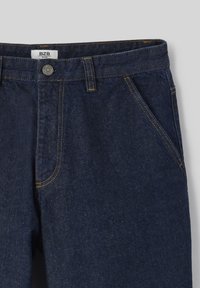 Jean en denim bleu foncé, avec un design classique à cinq poches, des coutures contrastées et une fermeture à bouton au niveau de la taille.