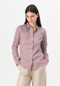 Striped shirt in red and white cotton with a button-up front, pointed collar, and long sleeves, paired with beige trousers.