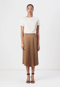 Brown pleated midi skirt with a textured finish, paired with a light-colored t-shirt featuring a logo, worn with black heeled sandals.